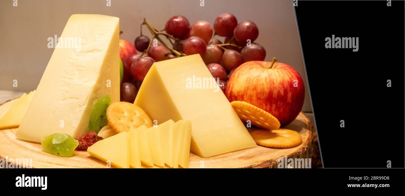 Queso gruyere con variedad de frutas y el cracker en placa de madera en