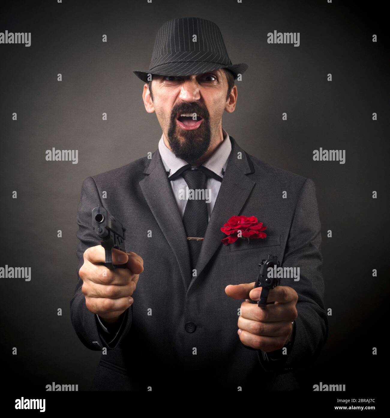 El elegante gángster o jefe mafioso de la vieja usanza en sombrero y traje  está apuntando con dos pistolas sobre fondo gris oscuro Fotografía de stock  - Alamy