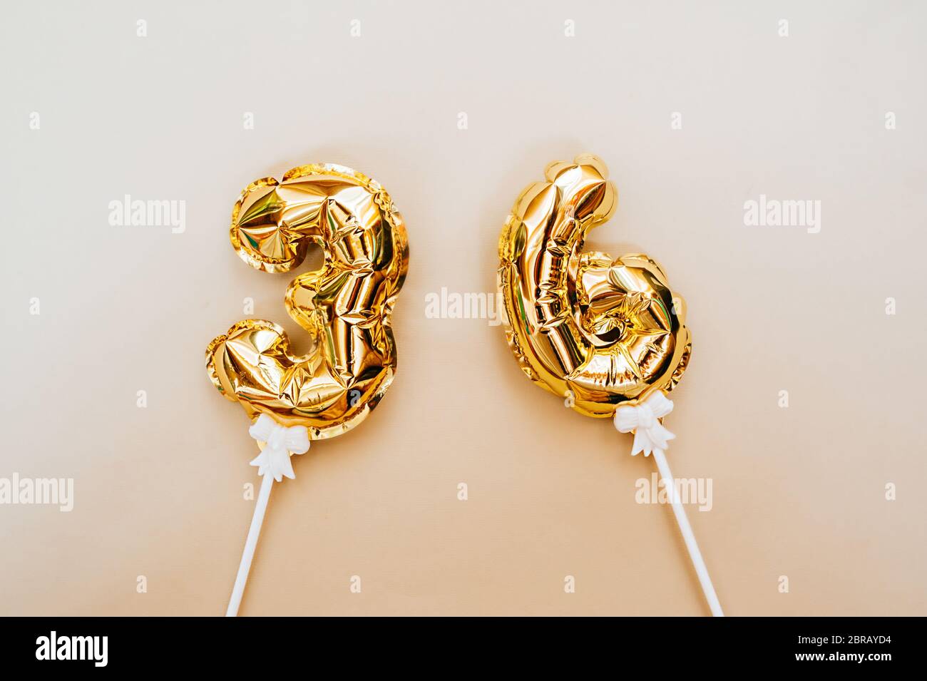 pequeños globos de oro de aluminio números 36 inflados con helio en un palo  blanco sobre un fondo beige delicado. brillante diseño de saludo de  vacaciones Fotografía de stock - Alamy