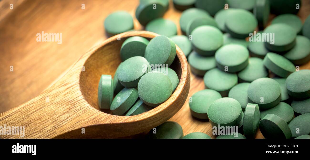 Algas verdes en comprimidos - clorela, espirulina en cuchara de madera sobre fondo de madera - diseño de banner de primer plano. Foto de stock