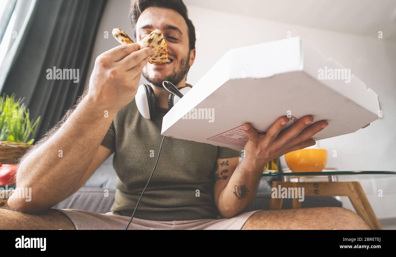 Hombre joven comiendo pizza en casa - Feliz hombre comiendo mientras juega videojuegos en la sala de estar - comida y jóvenes concepto de entretenimiento Foto de stock