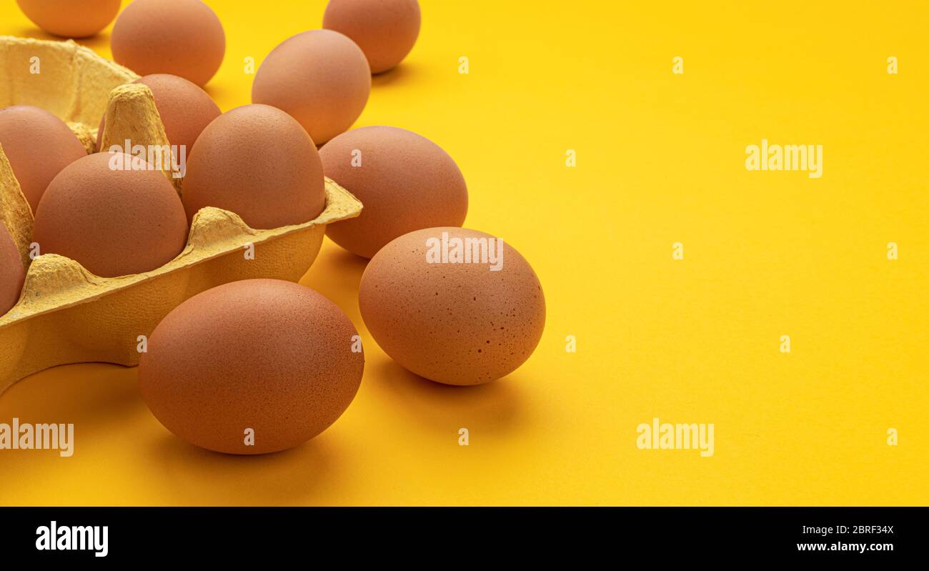 Huevos de pollo marrones en caja de cartón sobre fondo amarillo Foto de stock
