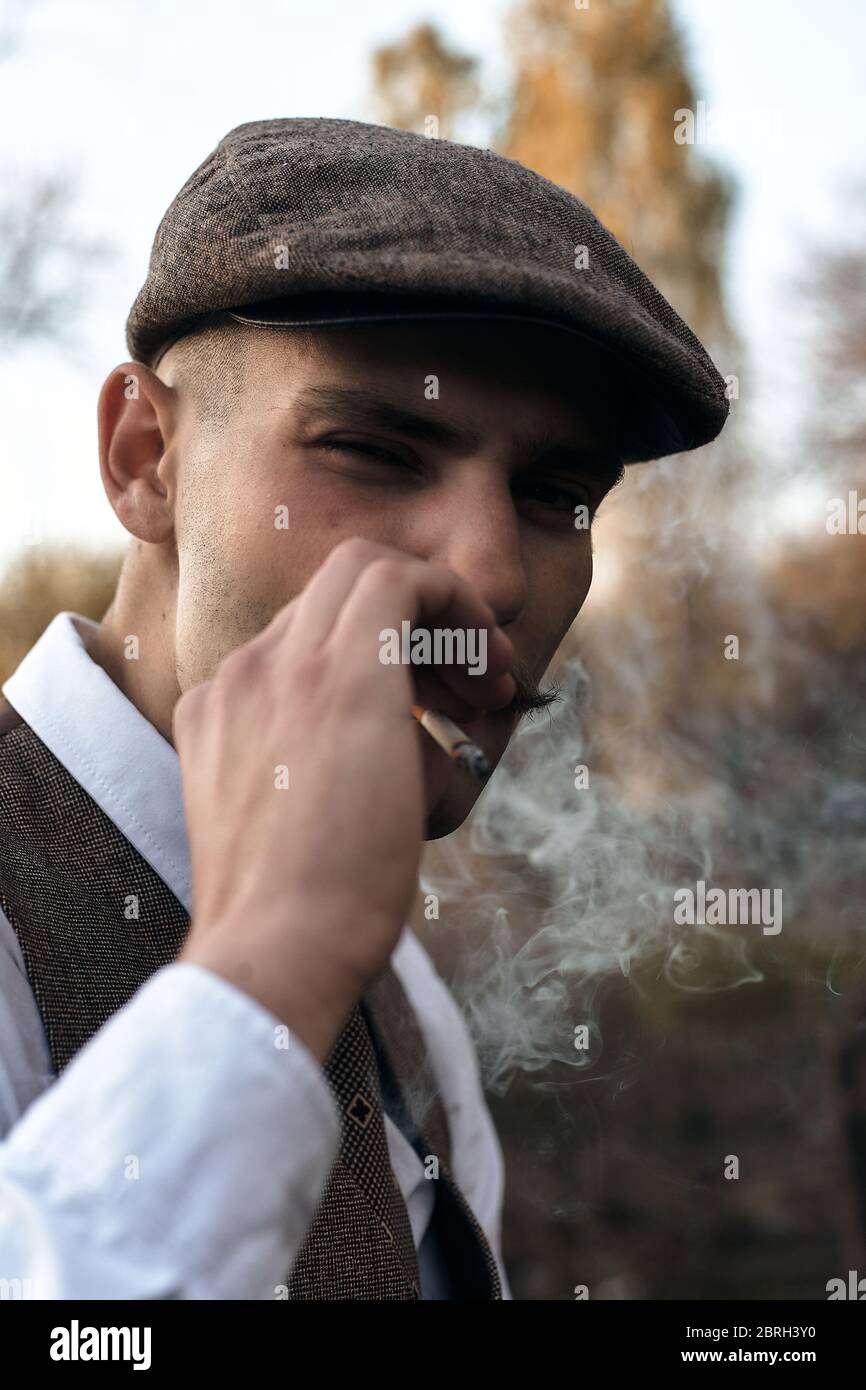 Retrato retro de 1920 de un gángster inglés con una gorra plana. Fuma un  cigarrillo en la calle Fotografía de stock - Alamy