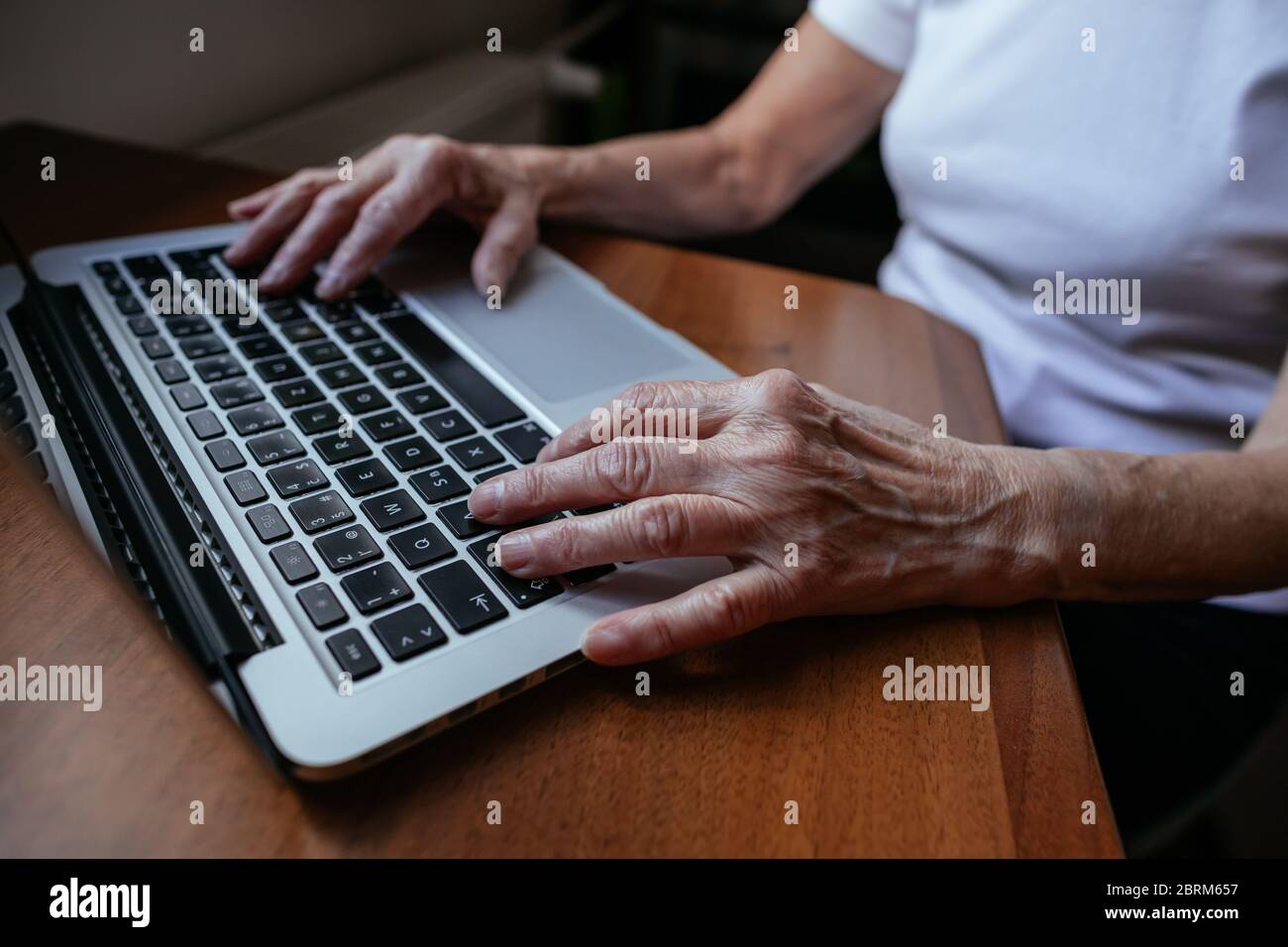 Primer plano de las manos de la anciana escribiendo en el ordenador portátil. La mano de una mujer anciana teclea en el cuaderno de casa. Foto de stock