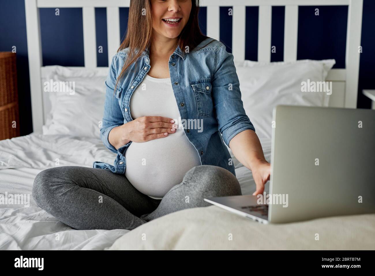 Mujer embarazada irreconocible usando un portátil en la cama Foto de stock