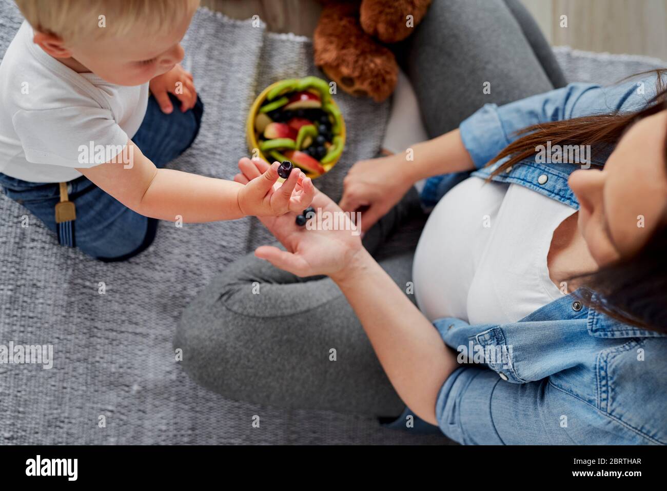 Madre convenciendo a su hijo bebé de comer algo de fruta Foto de stock