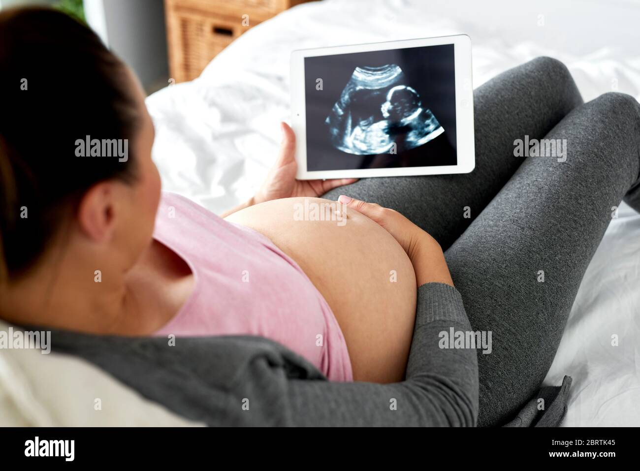 Mujer embarazada viendo el registro de ultrasonido en la tableta Foto de stock