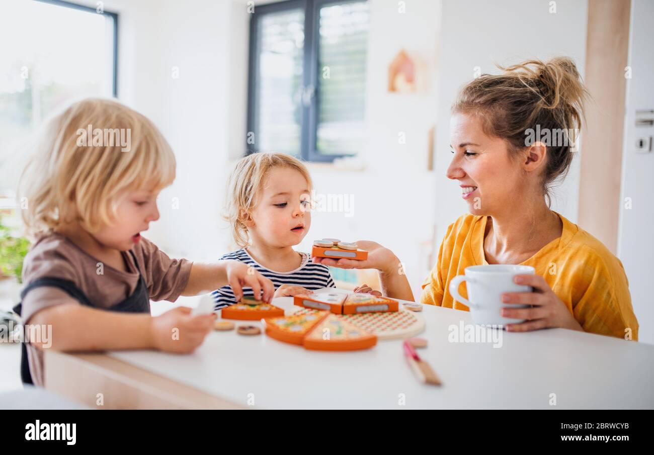 Madre con dos niños pequeños en el interior en el dormitorio jugando con juguetes. Foto de stock