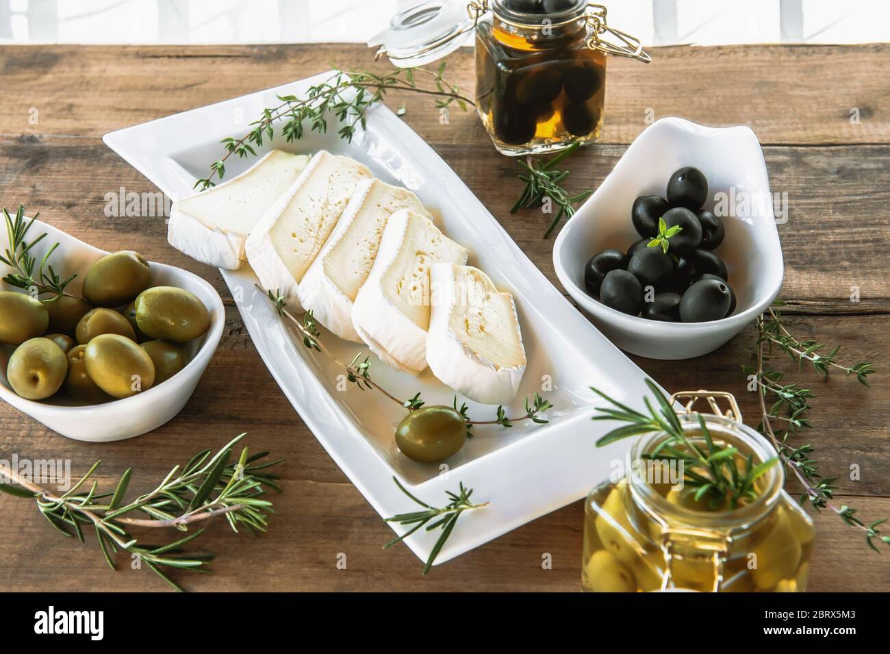 Las aceitunas son verdes y negras con queso suave con moho como brie,  Camembert con aceite de oliva y tomillo. Queso y aceitunas en un plato de  olivo Fotografía de stock -