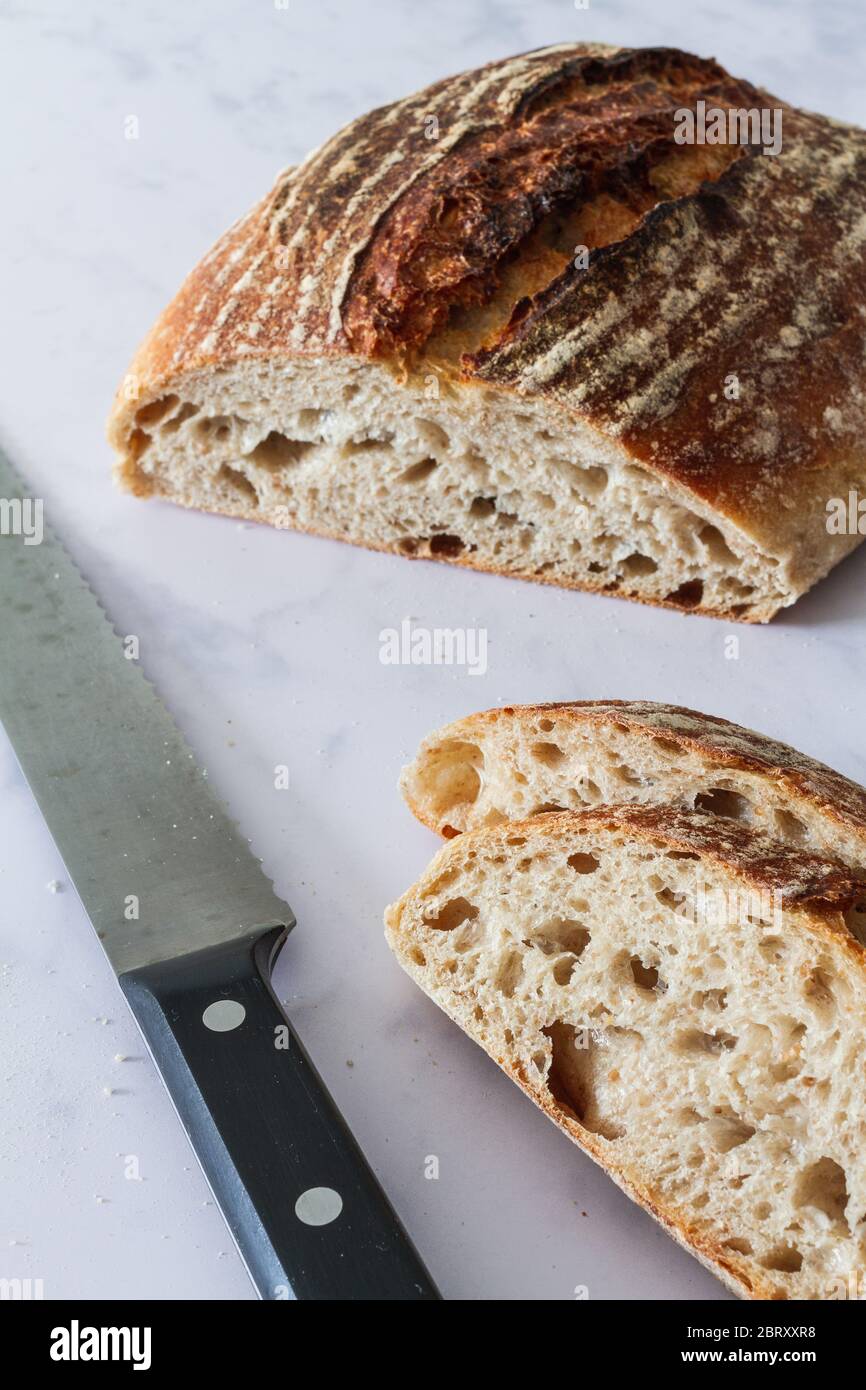 Pan de masa fermentada y rebanadas con un cuchillo de pan sobre fondo de mármol blanco Foto de stock