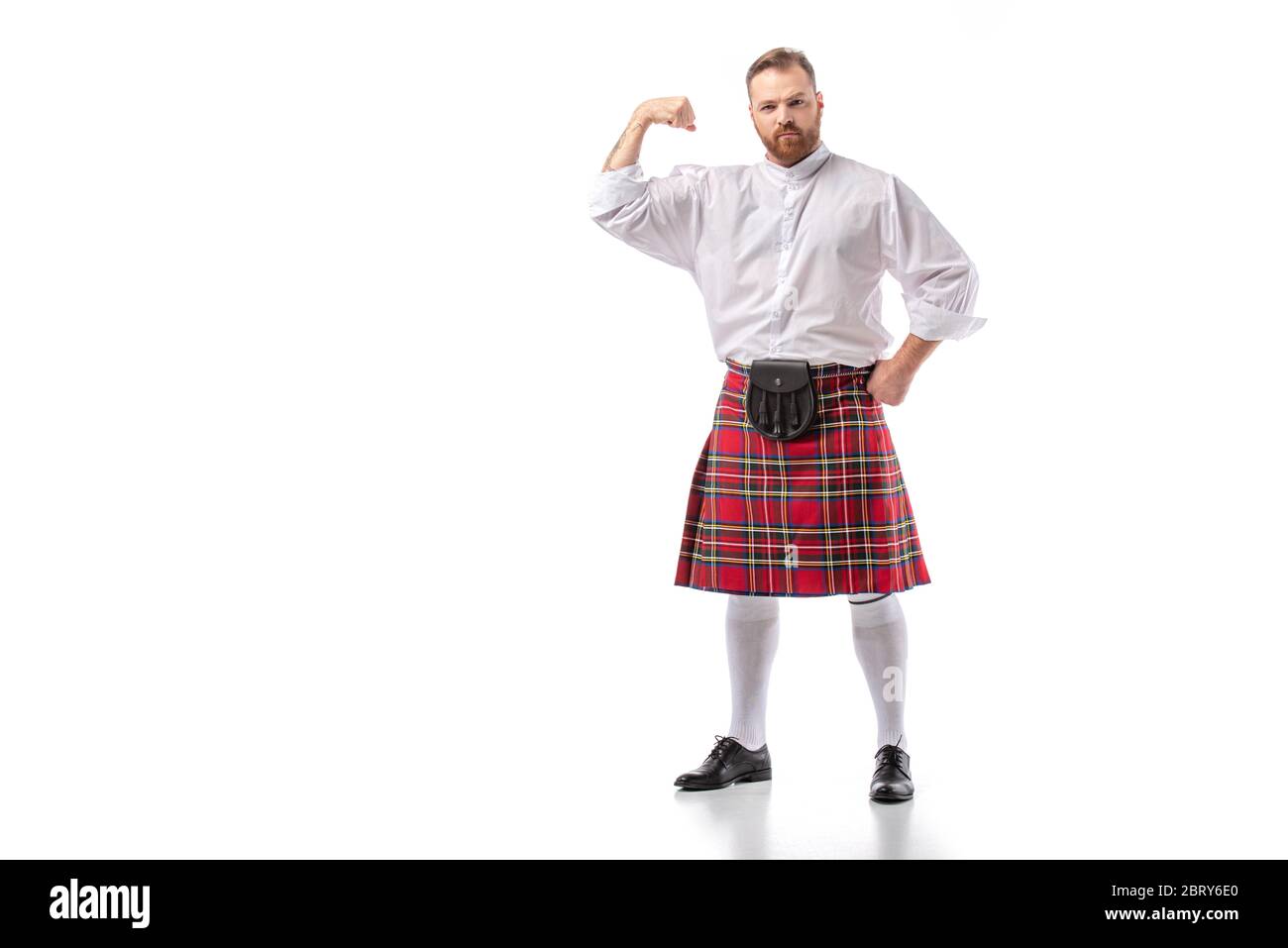 Fuerte escocesa pelirroja barbudo hombre en rojo tartán kilt mostrando bíceps sobre fondo blanco Foto de stock