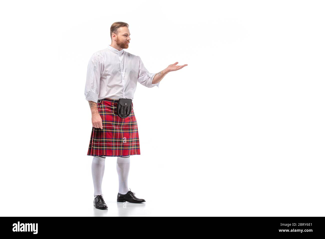 Escocesa pelirroja barbudo hombre en rojo tartán kilt apuntando con la mano sobre fondo blanco Foto de stock