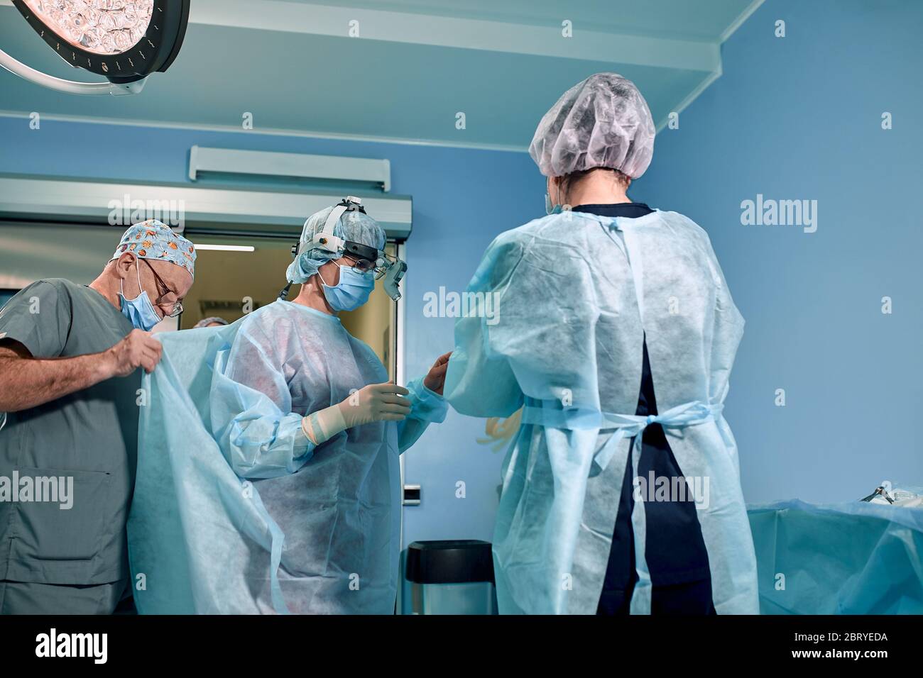 Un equipo de cirujanos se está preparando para la cirugía. Los cirujanos  usan ropa estéril antes de la cirugía con la ayuda de enfermeras, batas  estériles, guantes, máscaras, adentro Fotografía de stock -