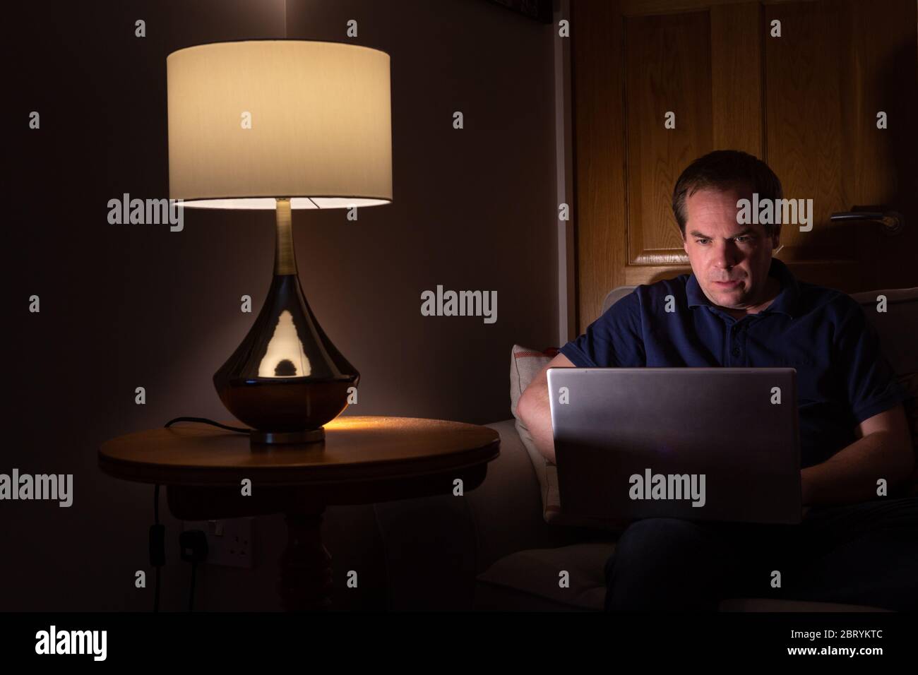 Hombre iluminado por la pantalla del portátil mientras trabajaba desde casa Foto de stock