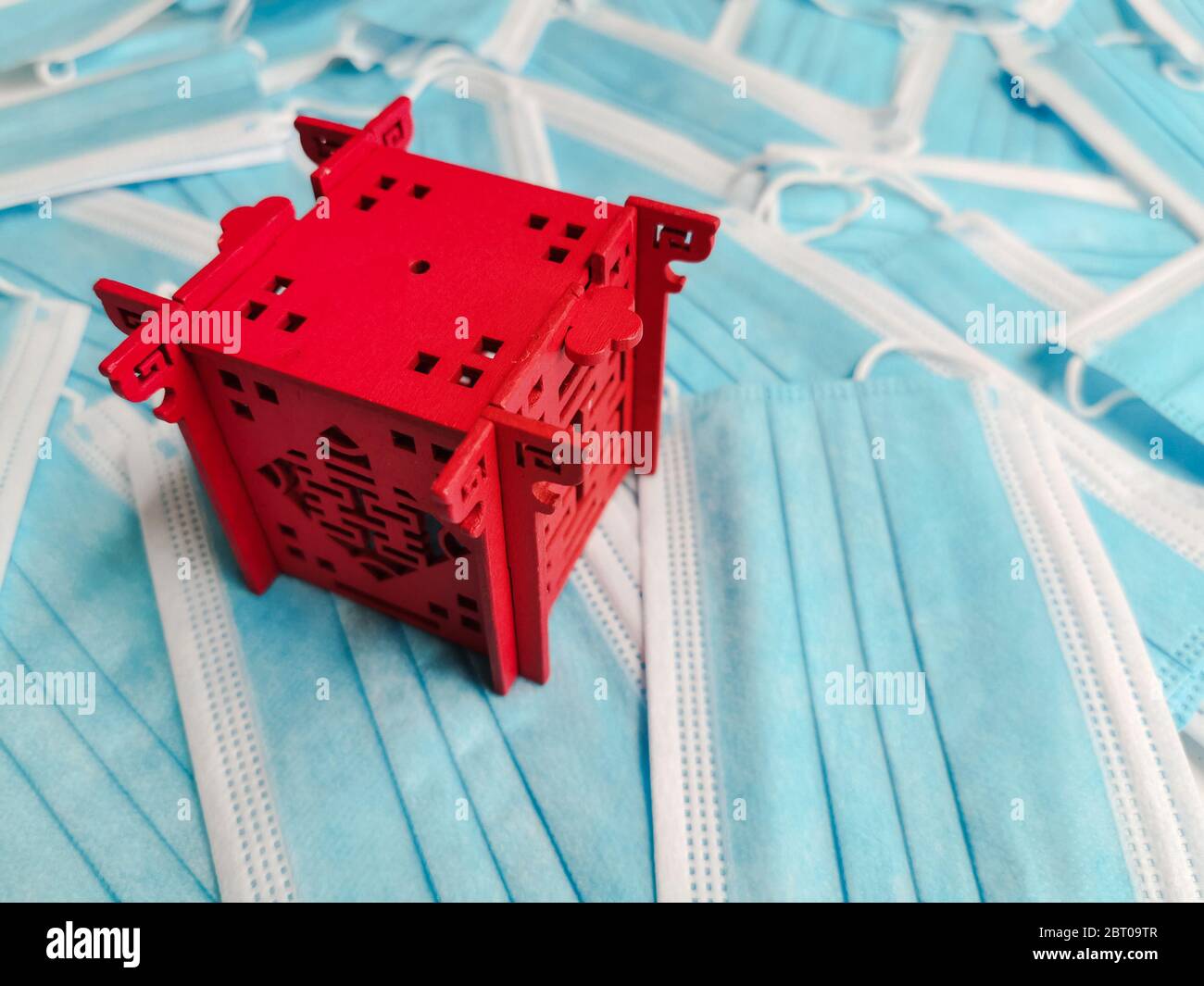 Pabellón rojo en miniatura que representa a China sobre un fondo de máscaras quirúrgicas desechables azules Foto de stock