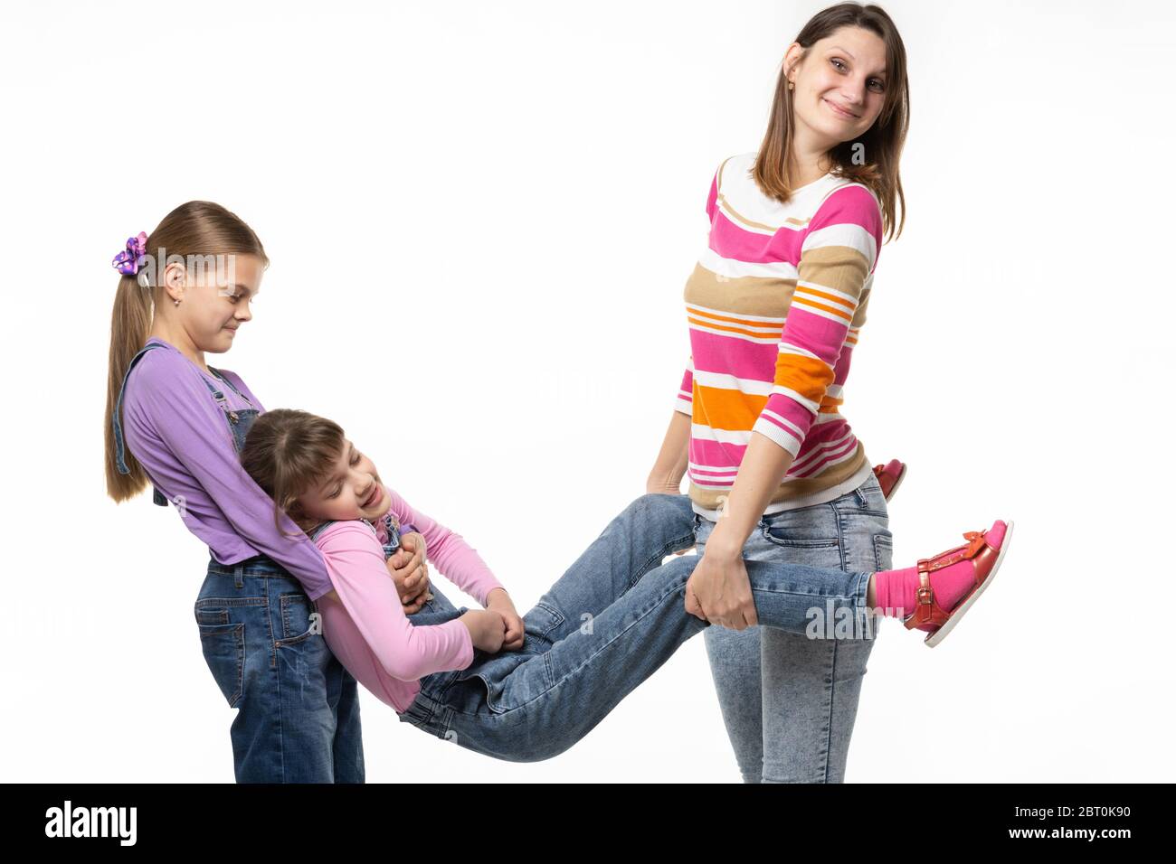 Mamá y la hija mayor tomaron a la hija menor por los brazos y las piernas Foto de stock