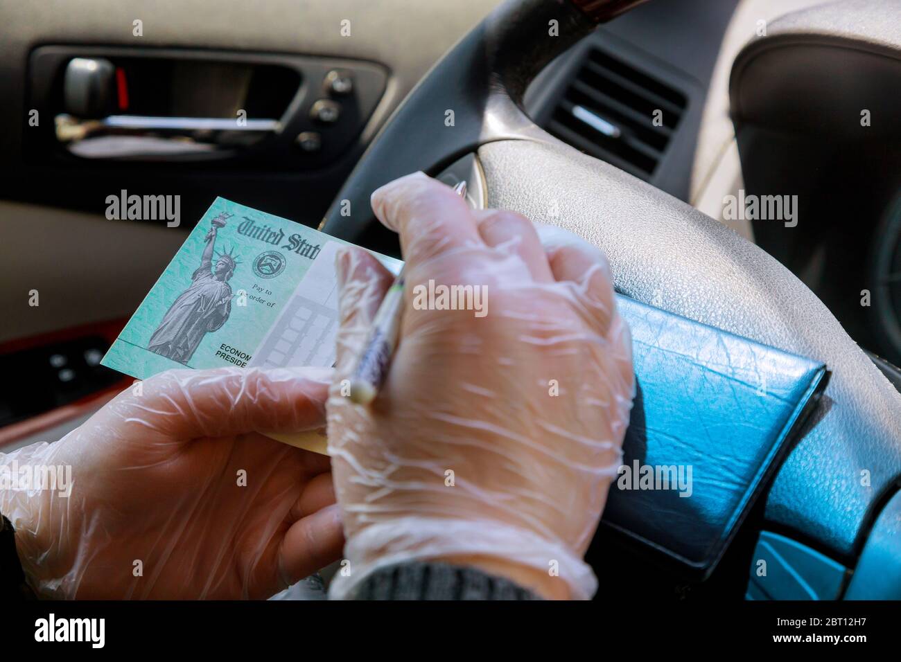 Escribir en cheque en blanco con en el coche con guantes al depositar el cheque de estímulo del gobierno con guantes para la seguridad Foto de stock