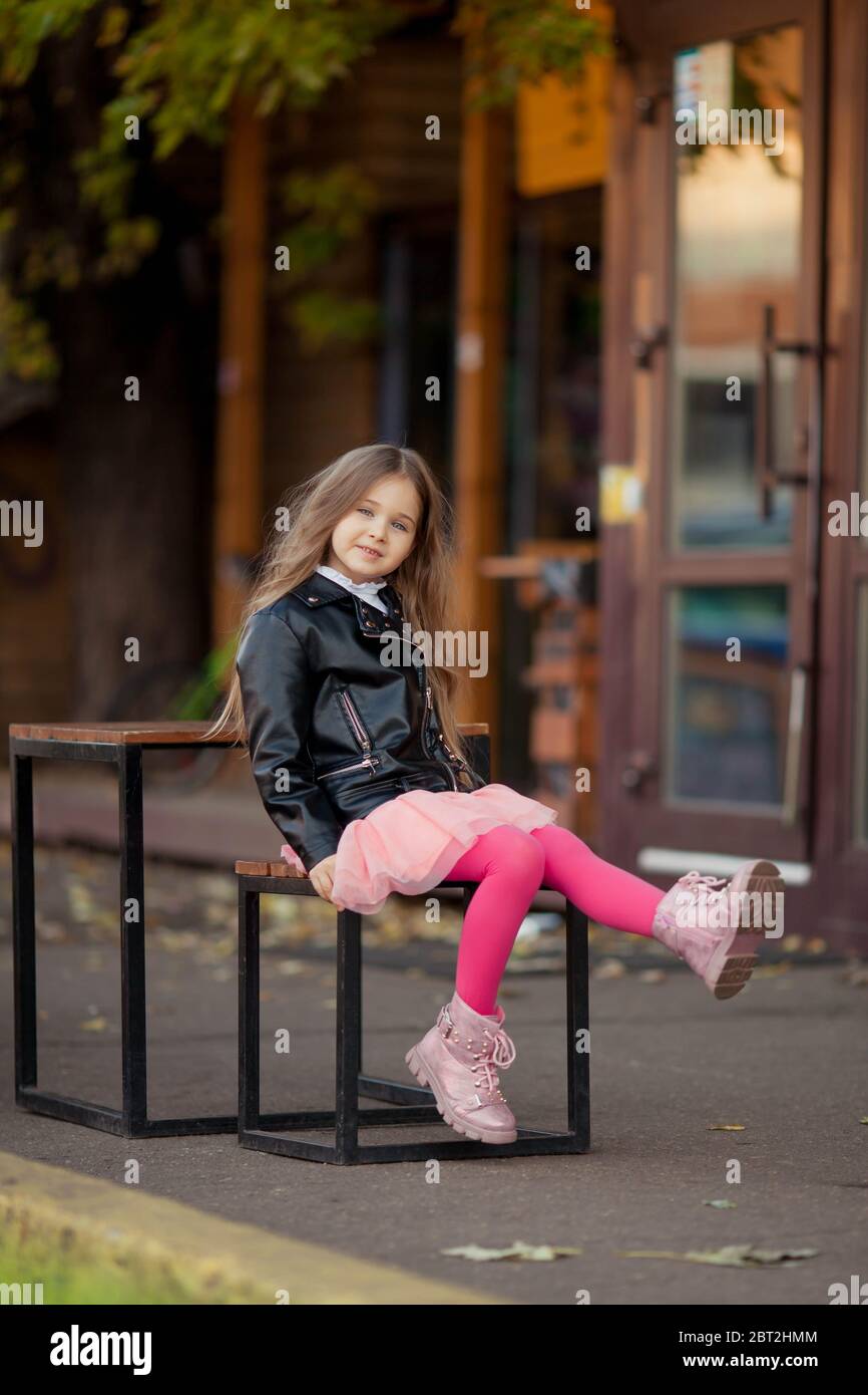 cute chica de pelo largo en una chaqueta de cuero que agitaba las piernas  en un banco Fotografía de stock - Alamy