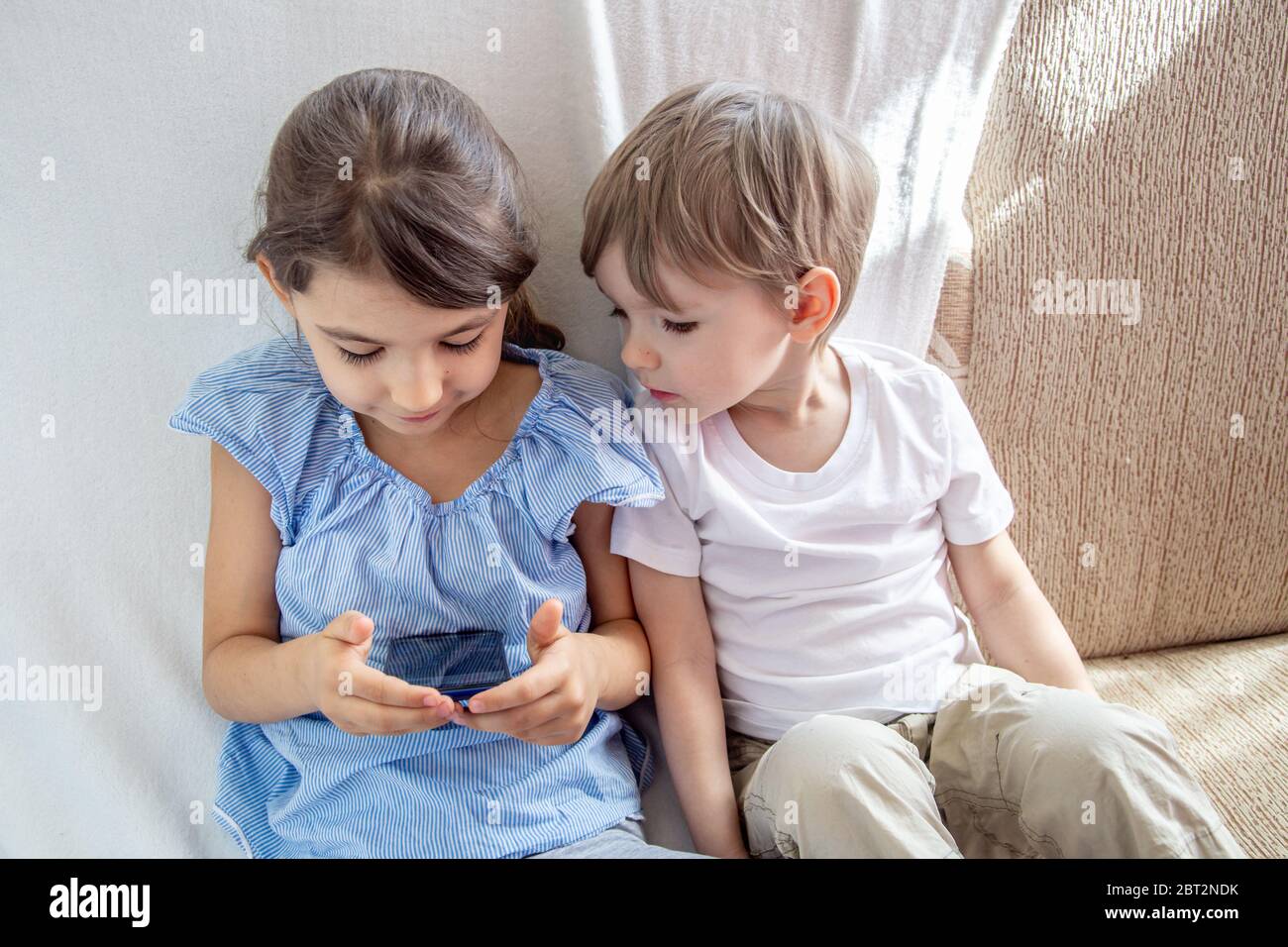 Los niños tienen un buen concepto de tiempo en casa. Cerrar hermano y hermana jugando con la tableta. Niños sentados en el sofá, jugando con la tableta. Los niños juegan un Foto de stock