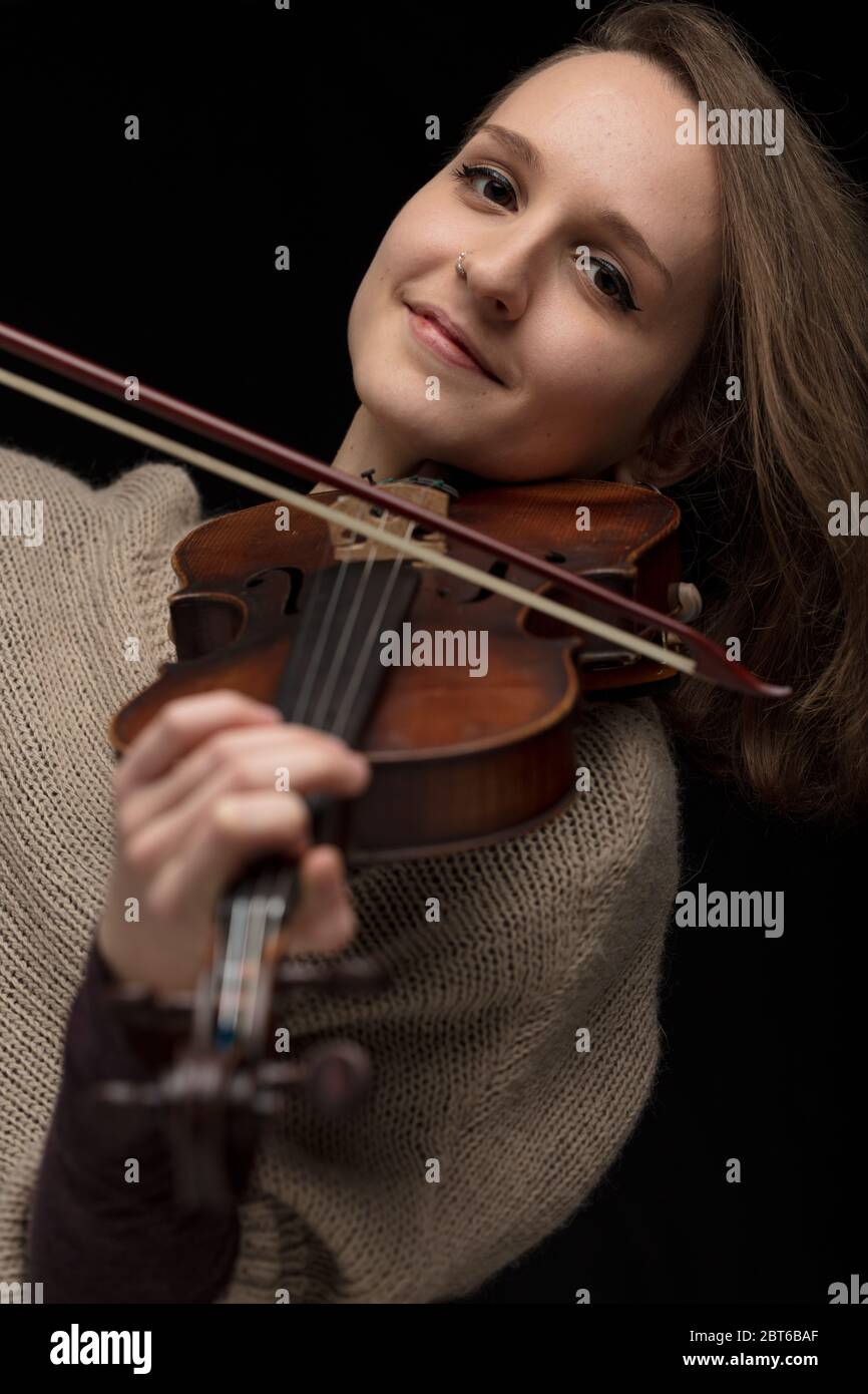 Violinista sonriente disfrutando tocando un violín barroco clásico en un retrato de primer plano con enfoque a su cara sobre un fondo negro Foto de stock