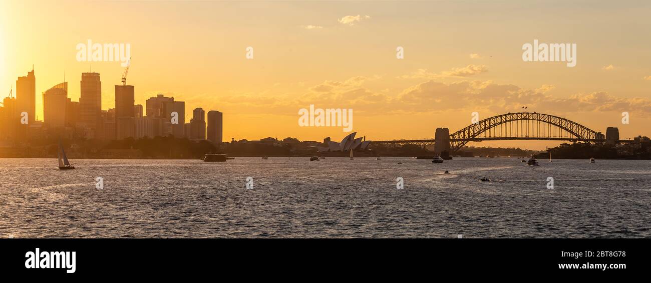 Vista panorámica del centro de Sydney, puente del puerto y la ópera con barcos navegando en la bahía al atardecer. Hermoso cielo naranja. Foto de stock