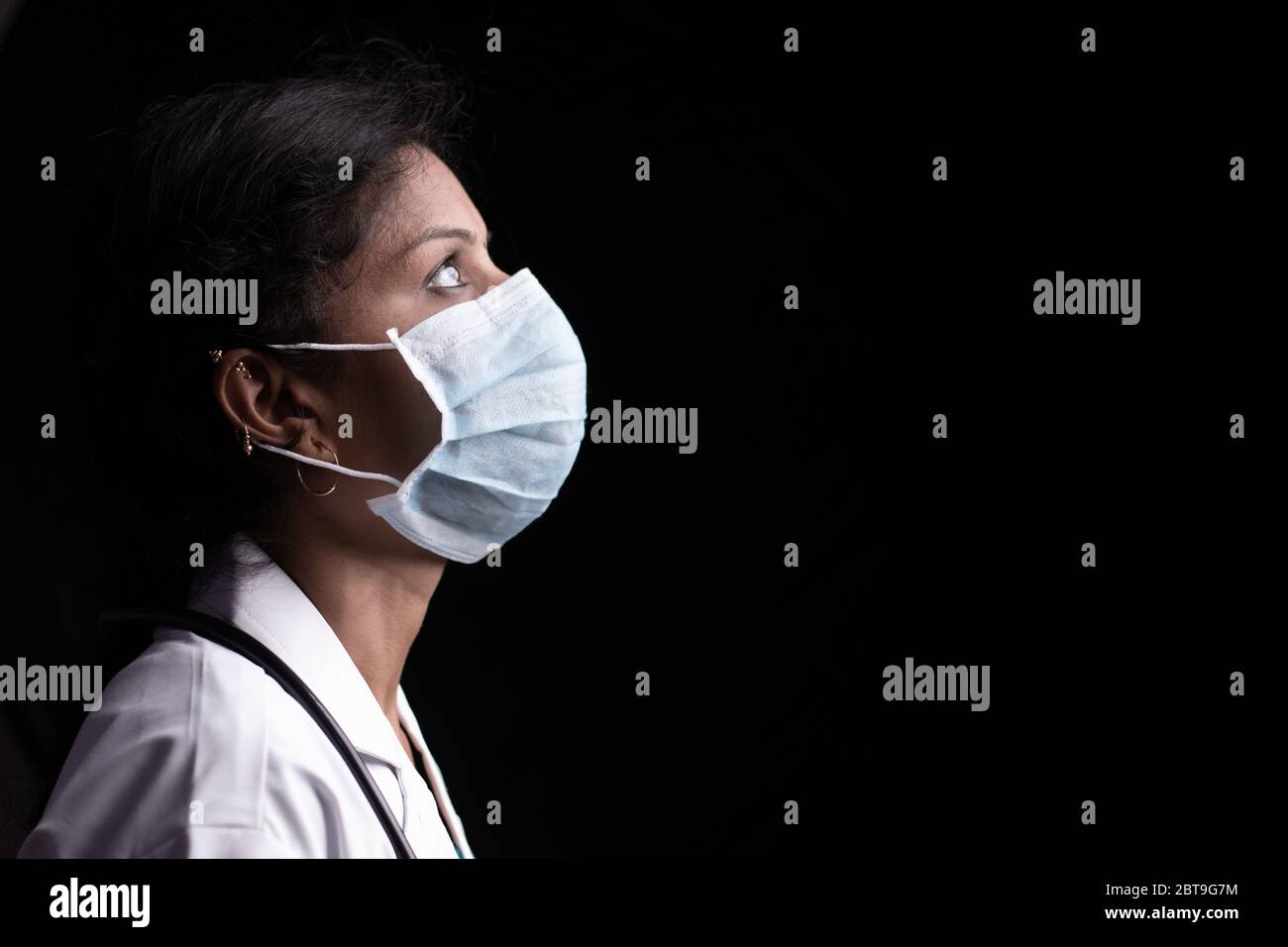 Perfil de la mujer joven médico con ojos abiertos en máscara médica sobre fondo negro buscando - concepto de esperanza y lucha para acabar con el coronavirus o. Foto de stock