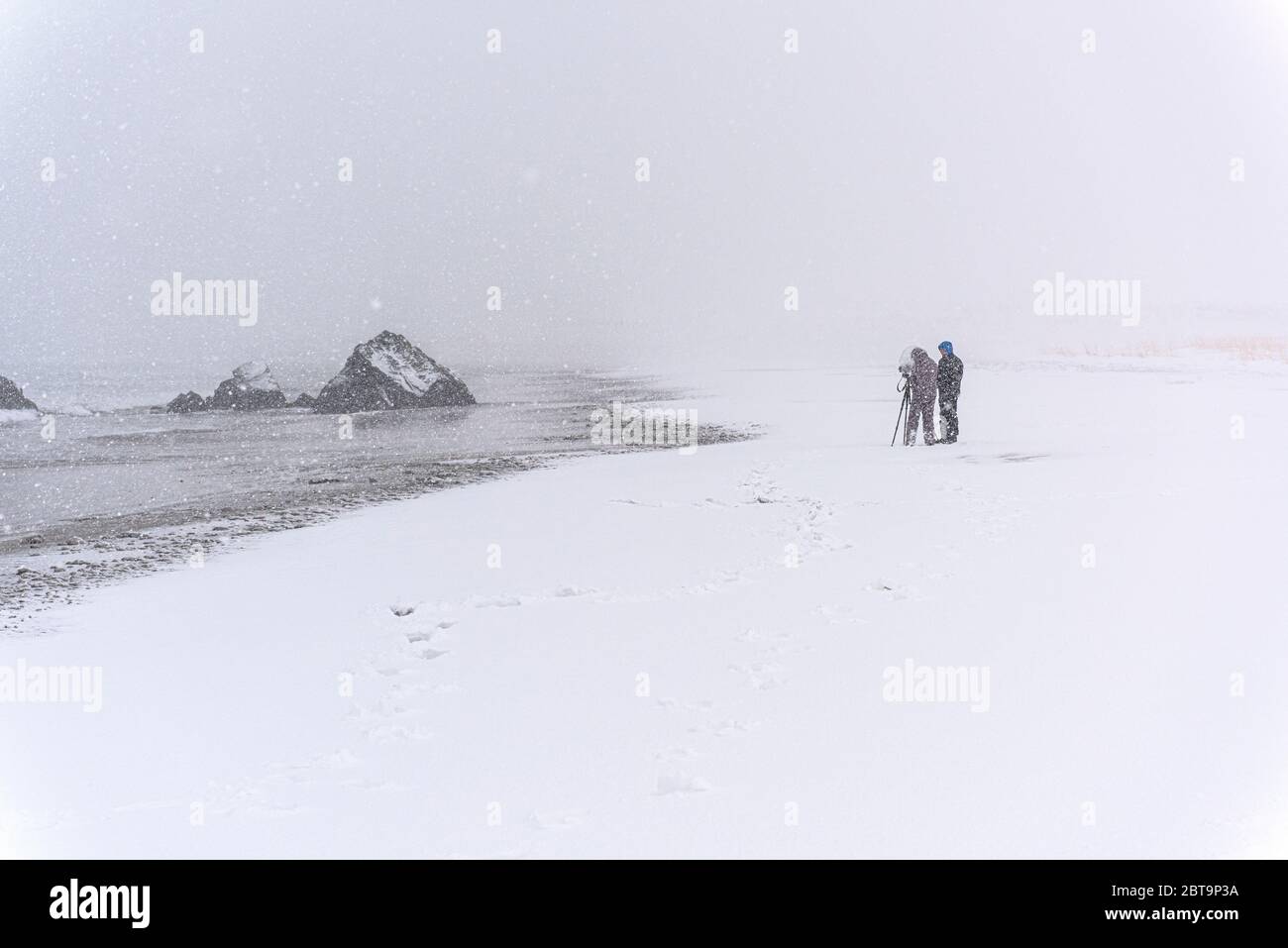 Persona irreconocible fotografiando una roca en la playa durante una tormenta de nieve ventosa Foto de stock