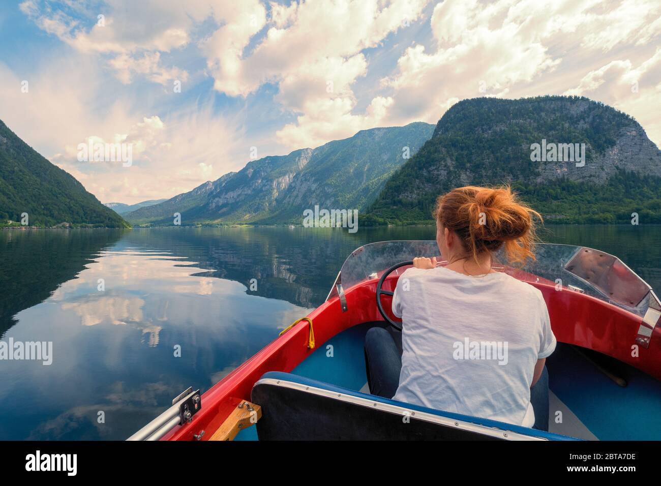 Crucero turístico femenino con pequeño barco rojo en el lago Hallstatt frente a un impresionante paisaje de montaña cerca de Hallstatt, región de Salzkammergut, OÖ, Austria Foto de stock