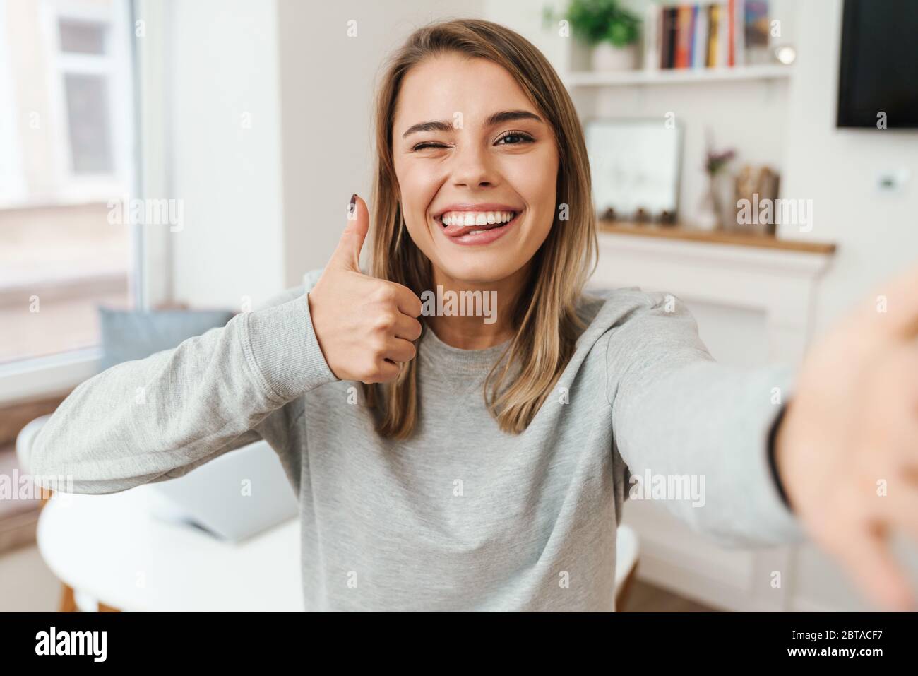 Foto De Una Joven Alegre Mostrando El Pulgar Hacia Arriba Y Guiñando Mientras Toma Una Foto 