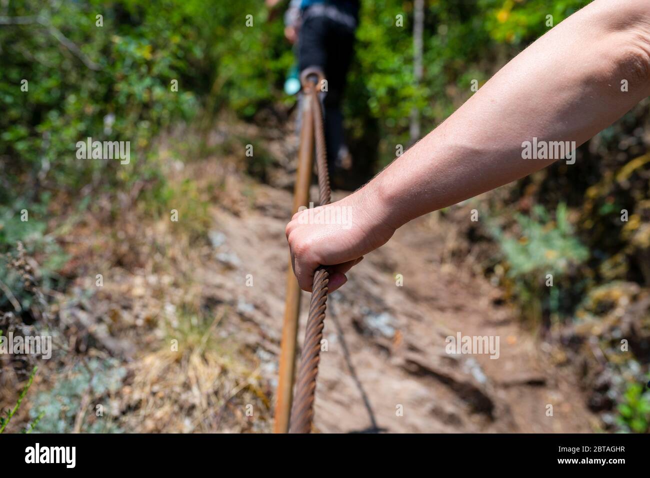 Una mano agarra la línea de metal firmemente en los viñedos en un empinado sendero de pizarra. Foto de stock