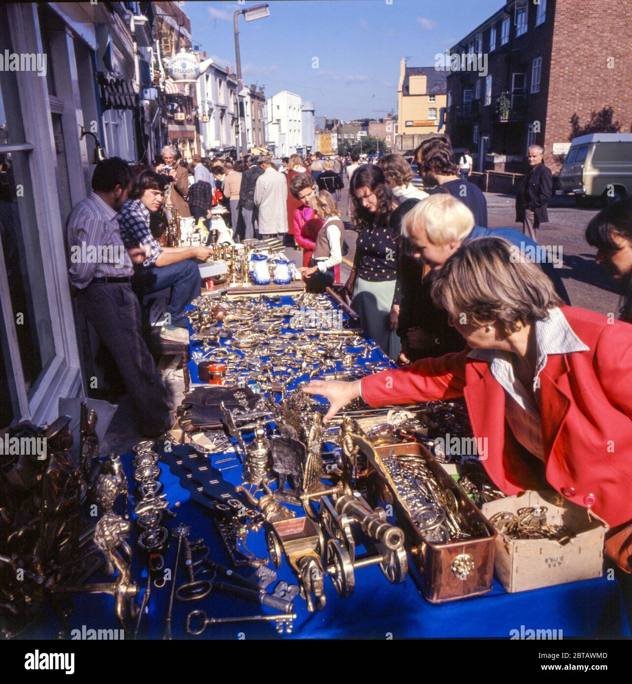 Los turistas, los distribuidores y los coleccionistas hojean las antigüedades y los curios de la mesa en Portobello Road en Nottiing Hill de Londres en el 1970s Foto de stock