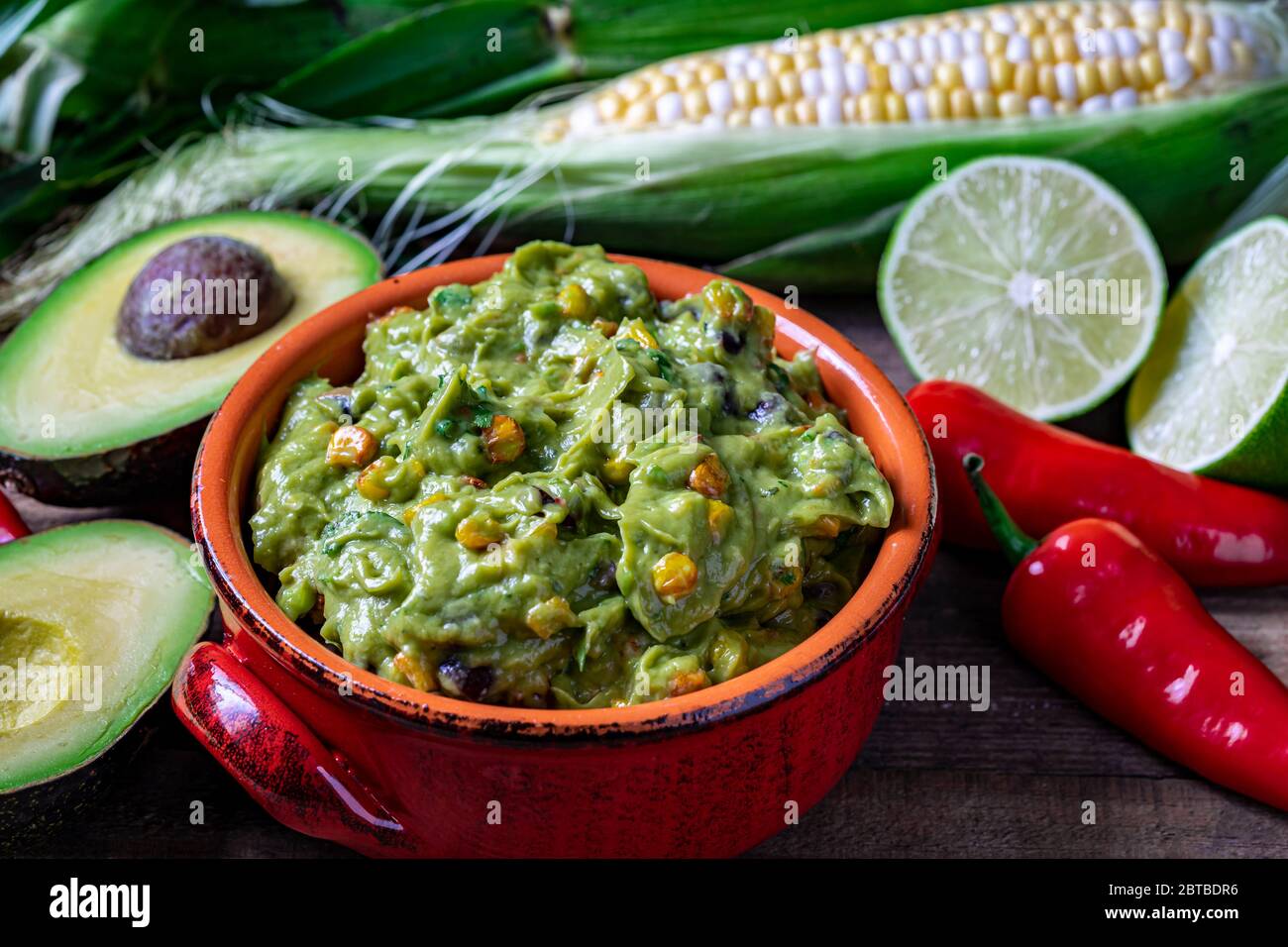 Salsa de guacamole con maíz asado e ingredientes crudos Foto de stock
