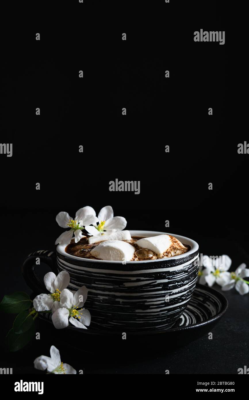 vida quieto, taza de café con malvaviscos y flores de primavera sobre un fondo negro, espacio vacío para el texto Foto de stock