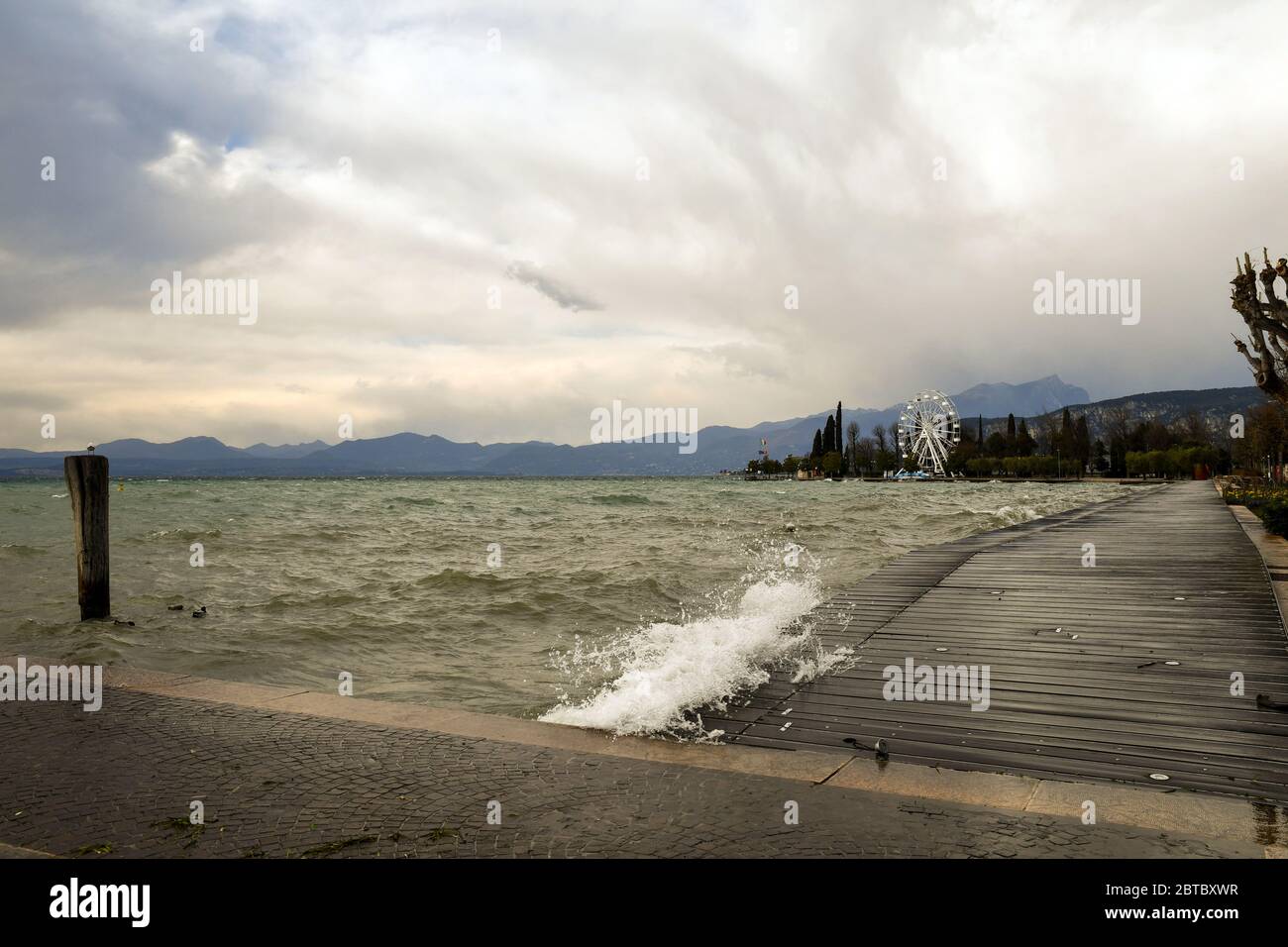 Vista panorámica del lago durante una tormenta con olas altas inundando el embarcadero de madera del paseo marítimo, Bardolino, Verona, Veneto, Italia Foto de stock