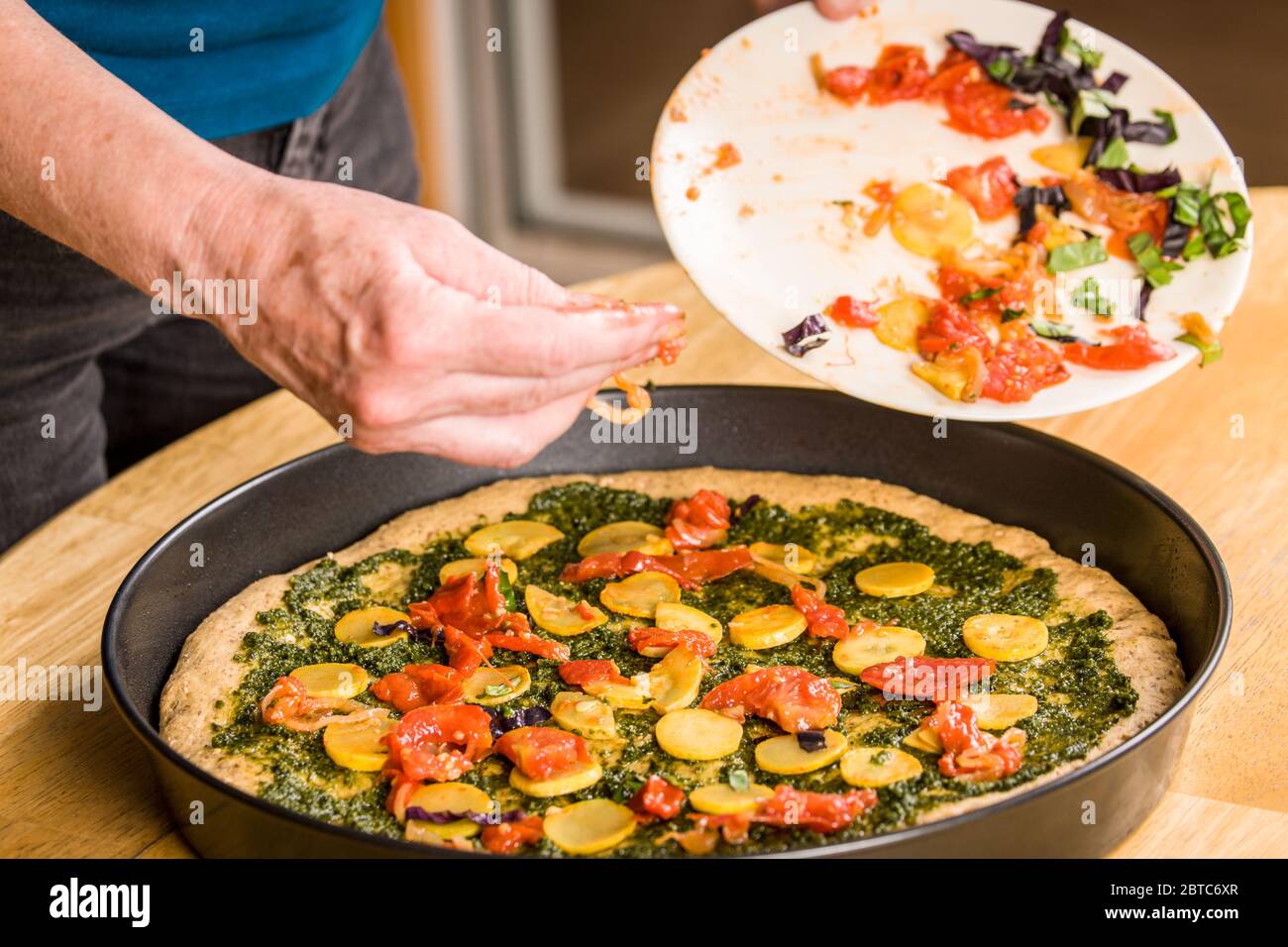 Mujer poniendo verduras salteadas encima de la pizza multigrano con salsa de pesto Foto de stock