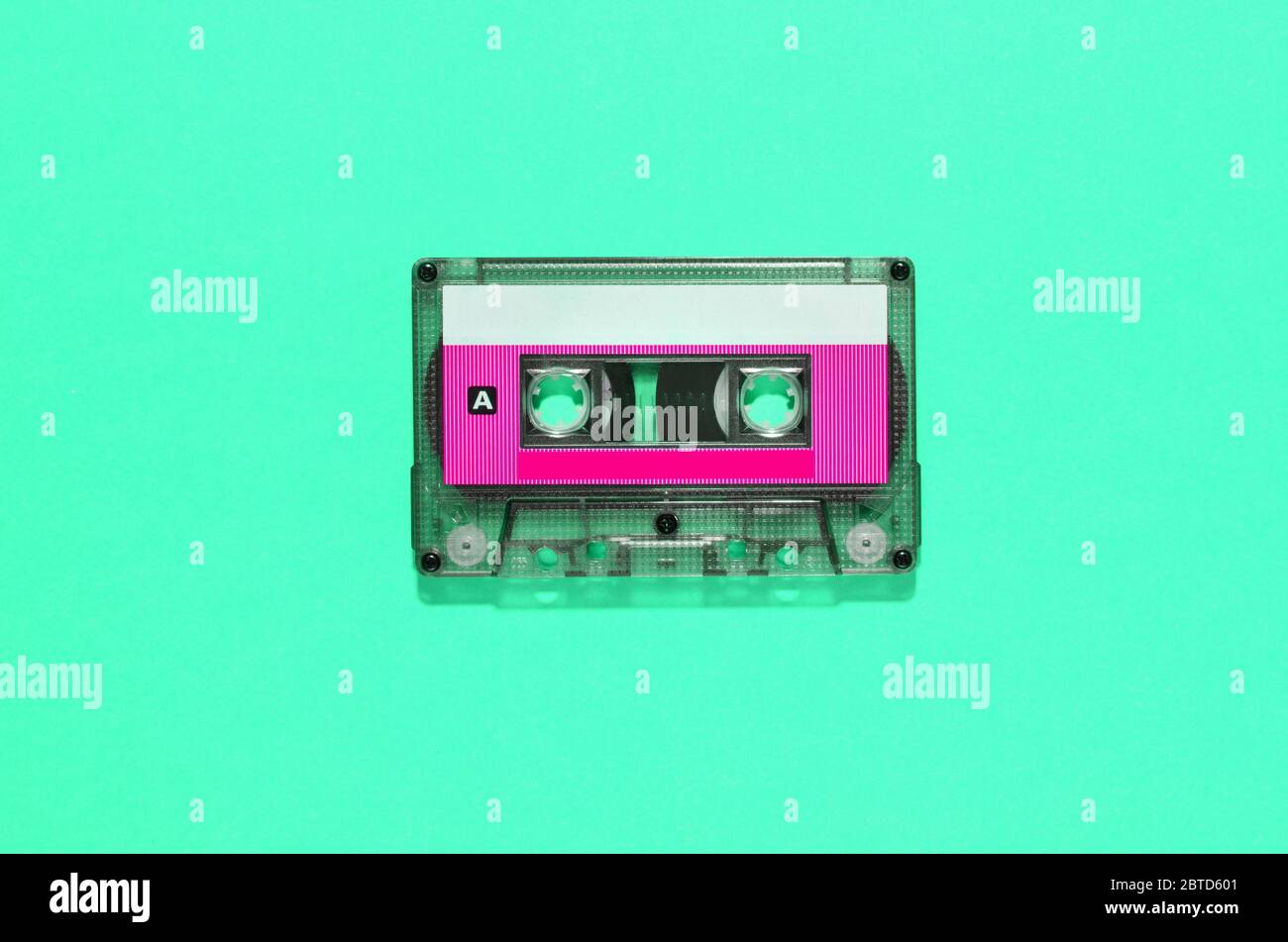 Cinta de audio vintage en casete de plástico con etiqueta en blanco de colores centrada sobre un fondo verde con espacio de copia en un plano de vida fija Foto de stock