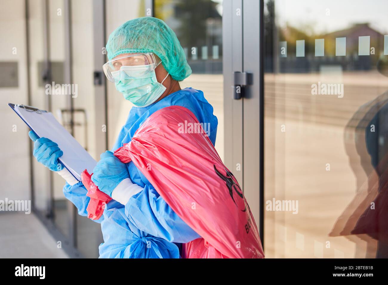 Limpiador con lista de verificación al verificar la eliminación de residuos peligrosos en la clínica durante la pandemia del coronavirus Foto de stock