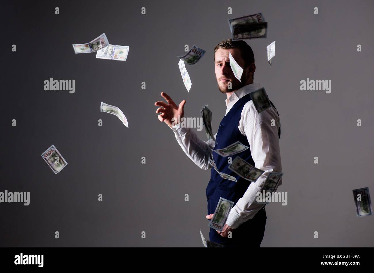 Hombre con ropa formal, hombre de negocios tirando dinero sobre fondo gris.  Concepto de riqueza y riqueza. Macho, empresario exitoso que pierde dinero.  Billetes, dólares en efectivo vuelan en el aire alrededor