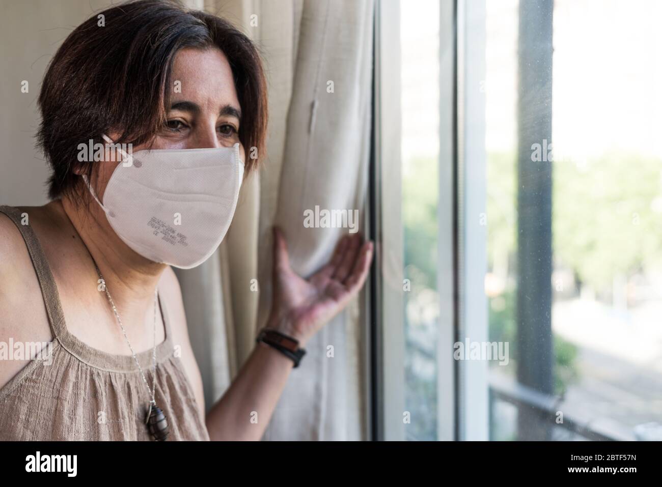 Mujer mirando a través de la ventana con máscara facial. Barcelona, España. Foto de stock