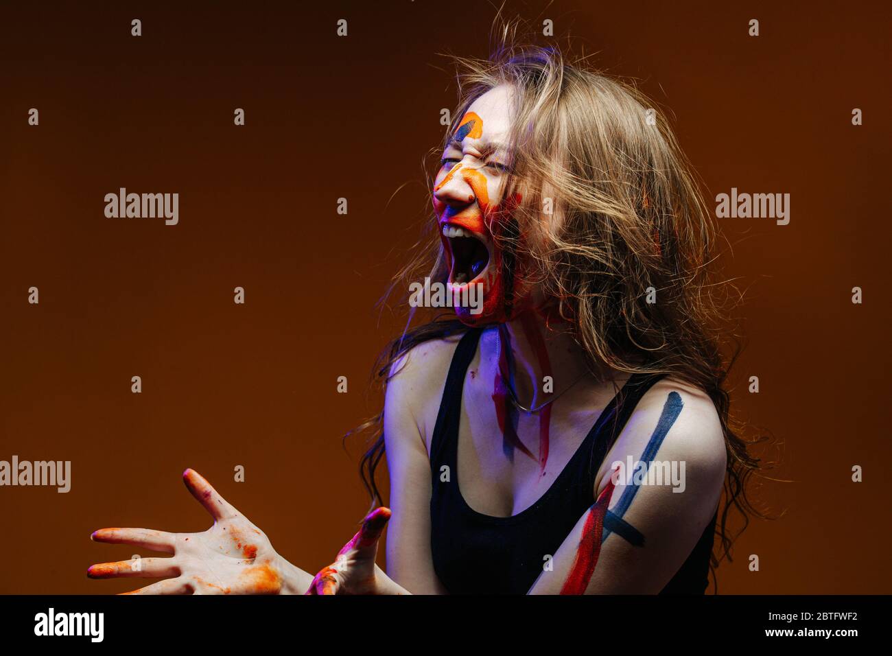 Mujer joven con cara pintada y brazos gritando con los ojos cerrados Foto de stock