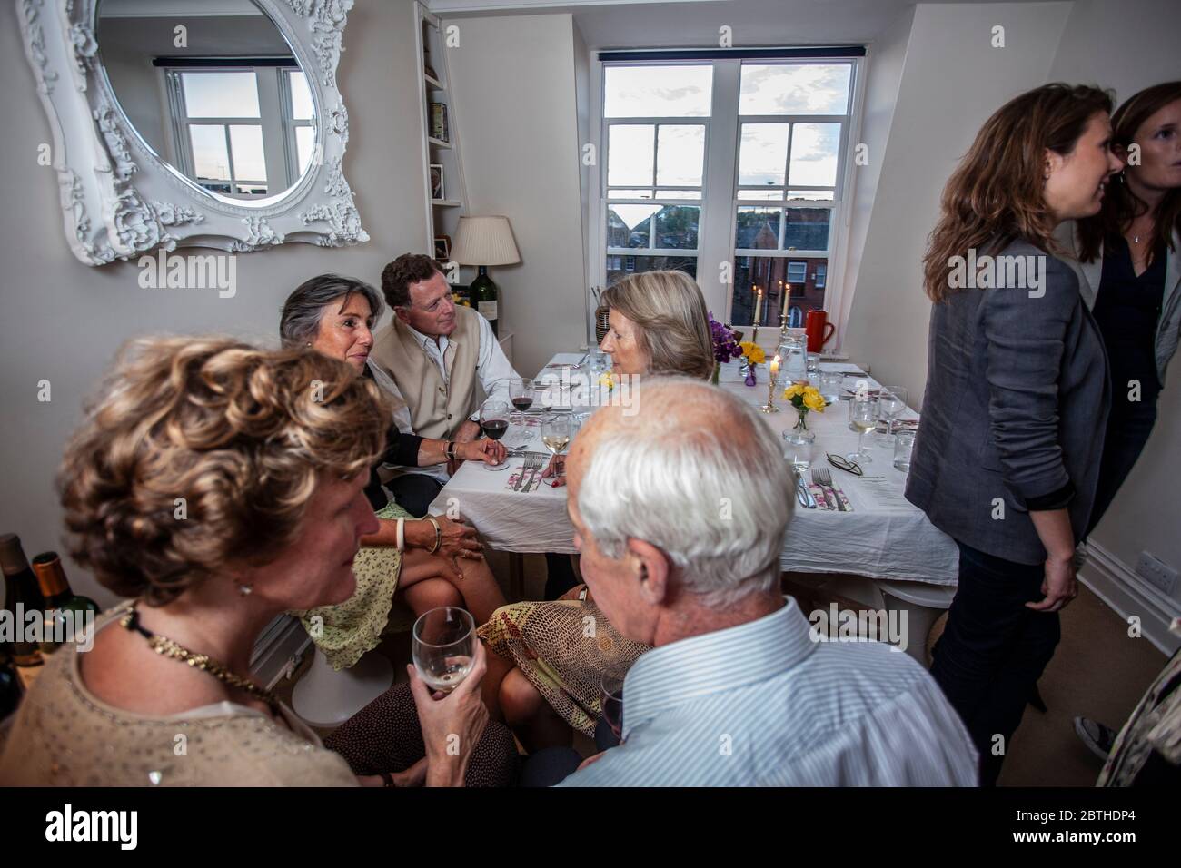 La gente se reúne alrededor de una mesa de cena en un apartamento de Londres para tomar una copa durante una cena, Londres, Inglaterra, Reino Unido Foto de stock
