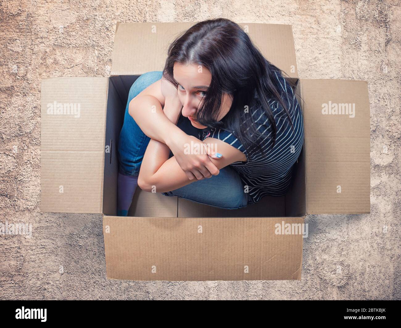 Mujer seria sentada en caja de cartón en suelo áspero. Espacio personal, aislamiento, introversión y tema de ansiedad Foto de stock