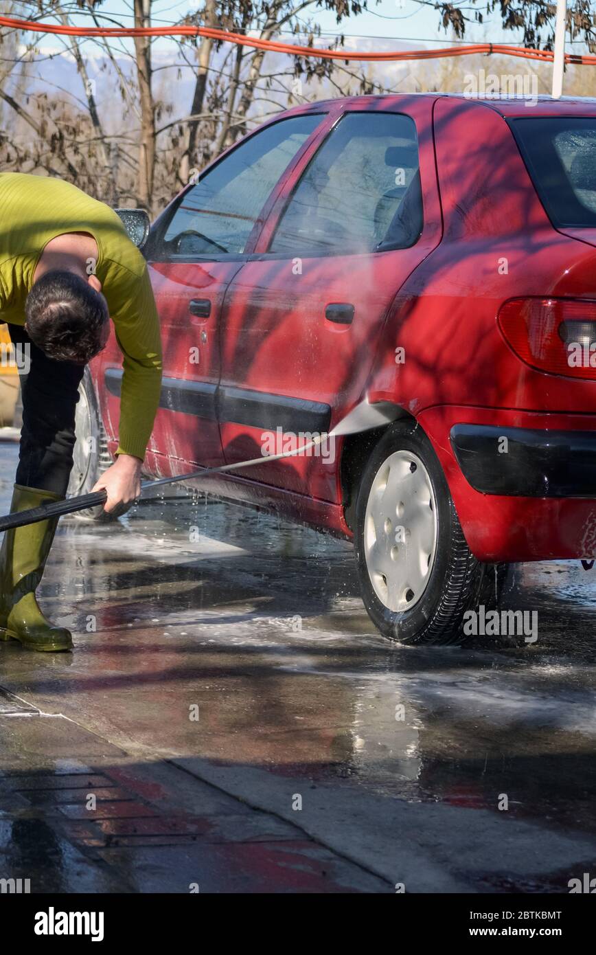 Hombre lavando un coche con un compresor de chorro de agua a alta presión Foto de stock