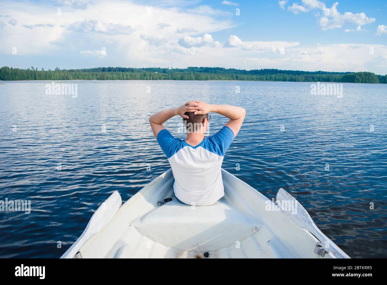 Hombre sentado en su espalda al barco y mirando el hermoso paisaje del lago en algún lugar en las profundidades de Finlandia. Concepto de vacaciones en el lago. Foto de stock