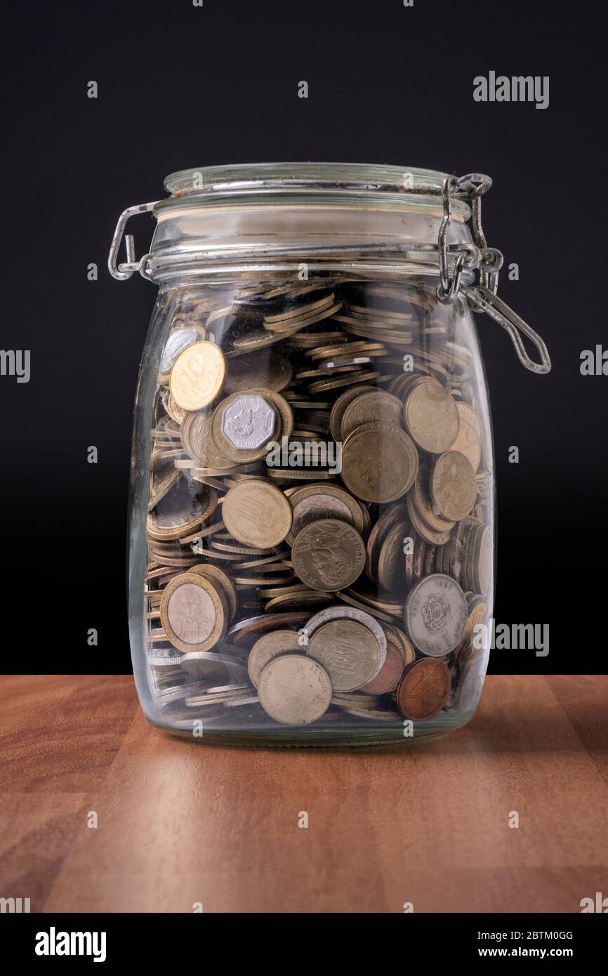 Monedas dentro de un recipiente de vidrio lleno de dinero Foto de stock
