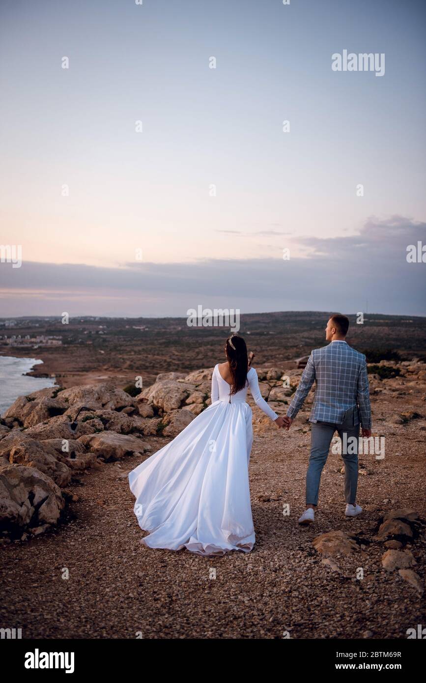 Vista Posterior De La Joven Pareja De Bodas Novia Y Novio Caminando En Una Playa Rocosa Por La Noche En Chipre Hermoso Dia De Boda Tiempo Para Dos Fotografia De Stock