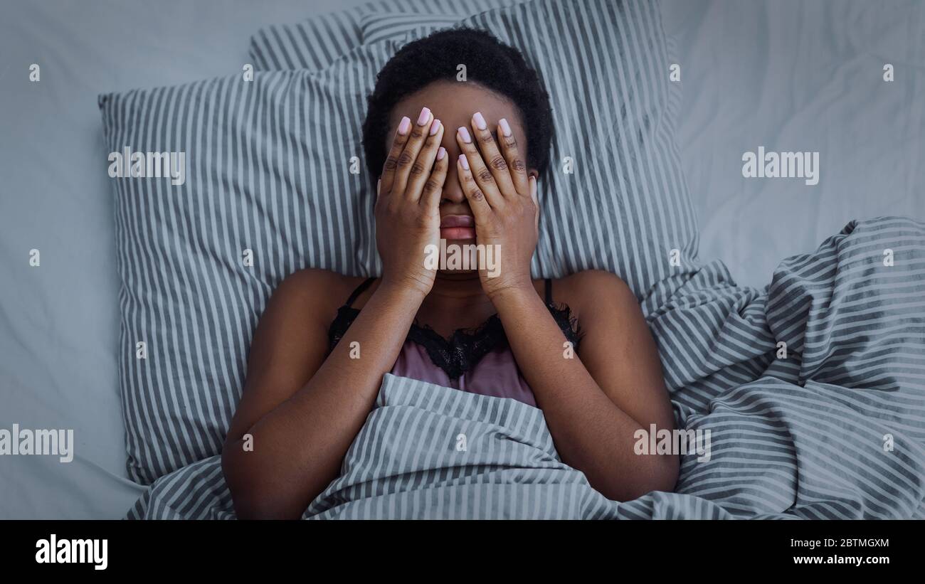 Una niña afroamericana cerró los ojos con las manos en la cama Foto de stock