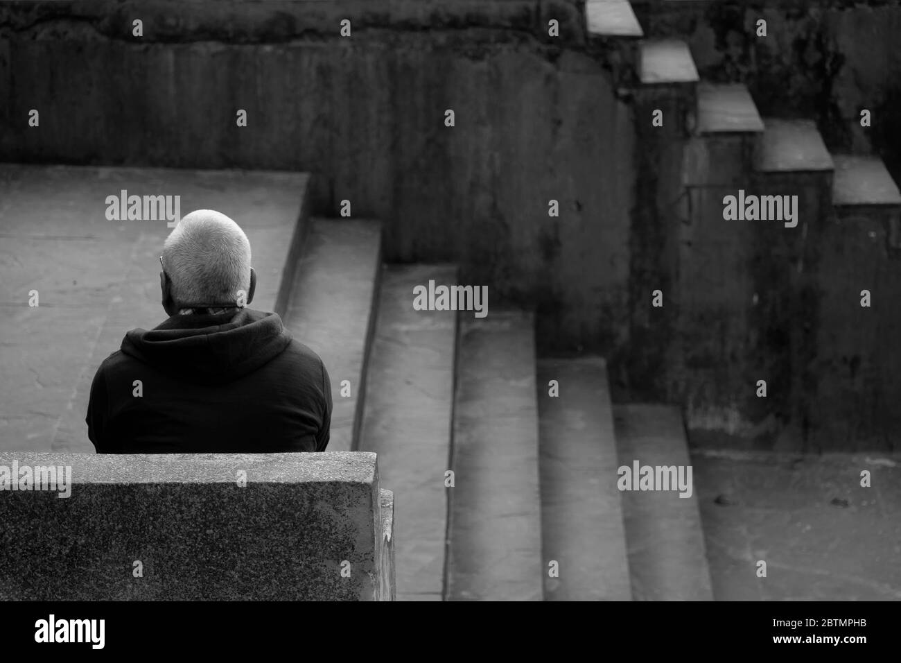 Un hombre viejo con cara oculta sentado solo por las escaleras Foto de stock