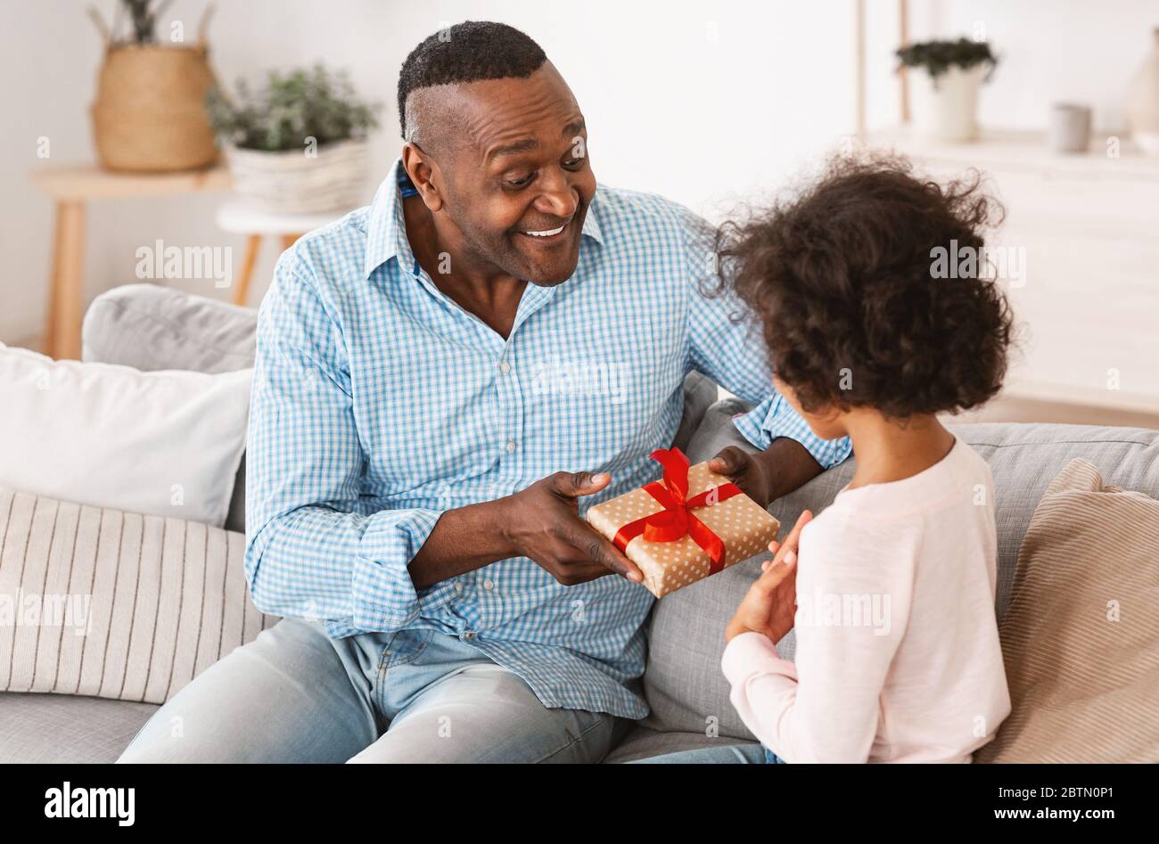 Mejor regalo de cumpleaños. Un hombre afroamericano anciano que da el regalo a una chica curly en casa Foto de stock
