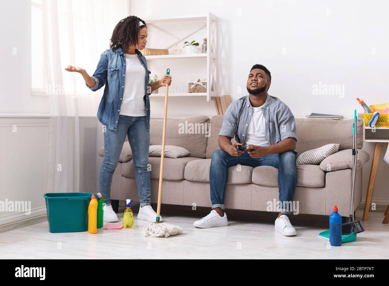 Disgustada Mujer Africana culpar a marido perezoso jugando videojuegos mientras limpiaba Foto de stock